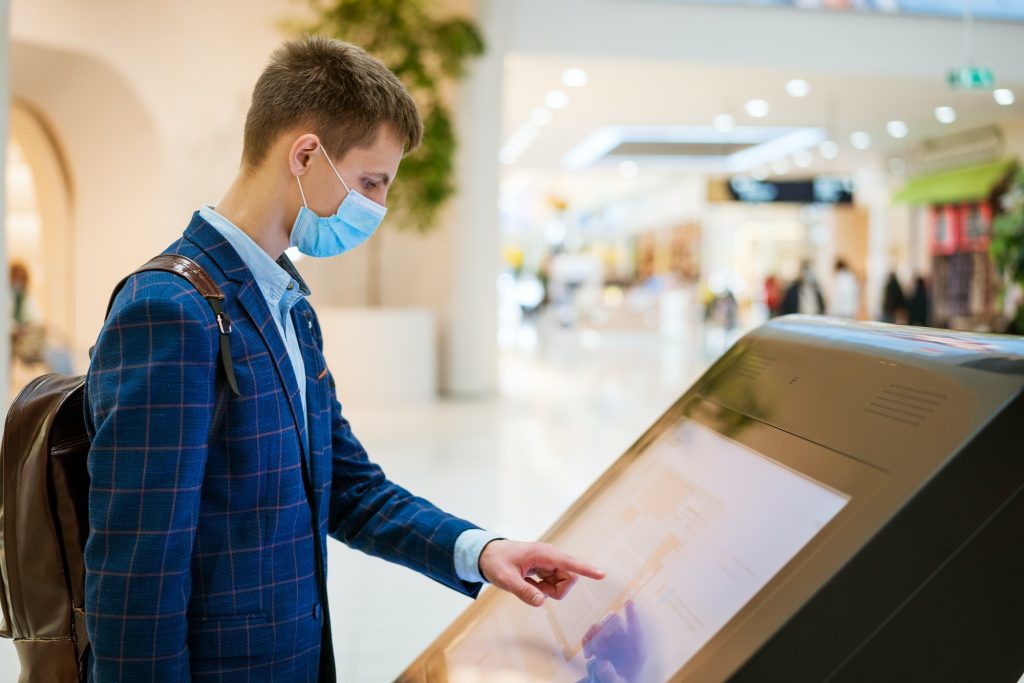 young man in the mall looks at the monitor in a mask